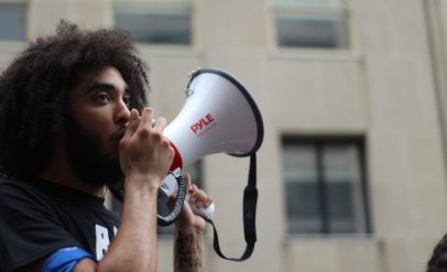 selective focus photography of man holding loudspeaker beside building