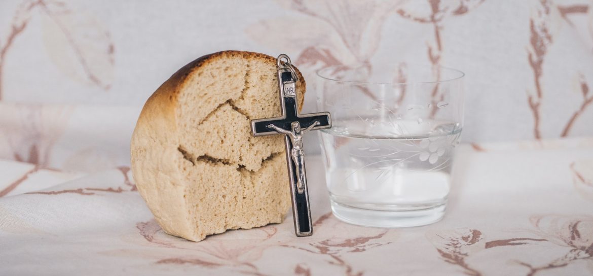 Crucifix pendant on bread beside glass