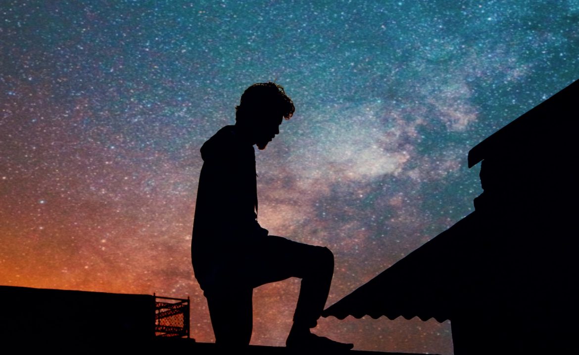 silhouette of man standing on roof under blue sky