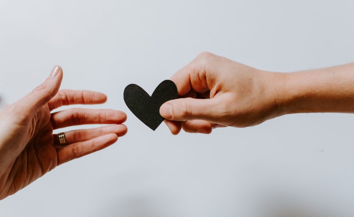 person reaching black heart cutout paper